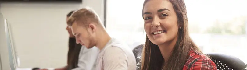 A female student looking at the camera with people working behind her