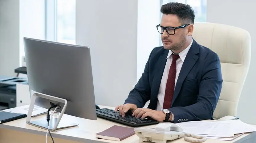 A man wearing a suit and tie working at a computer