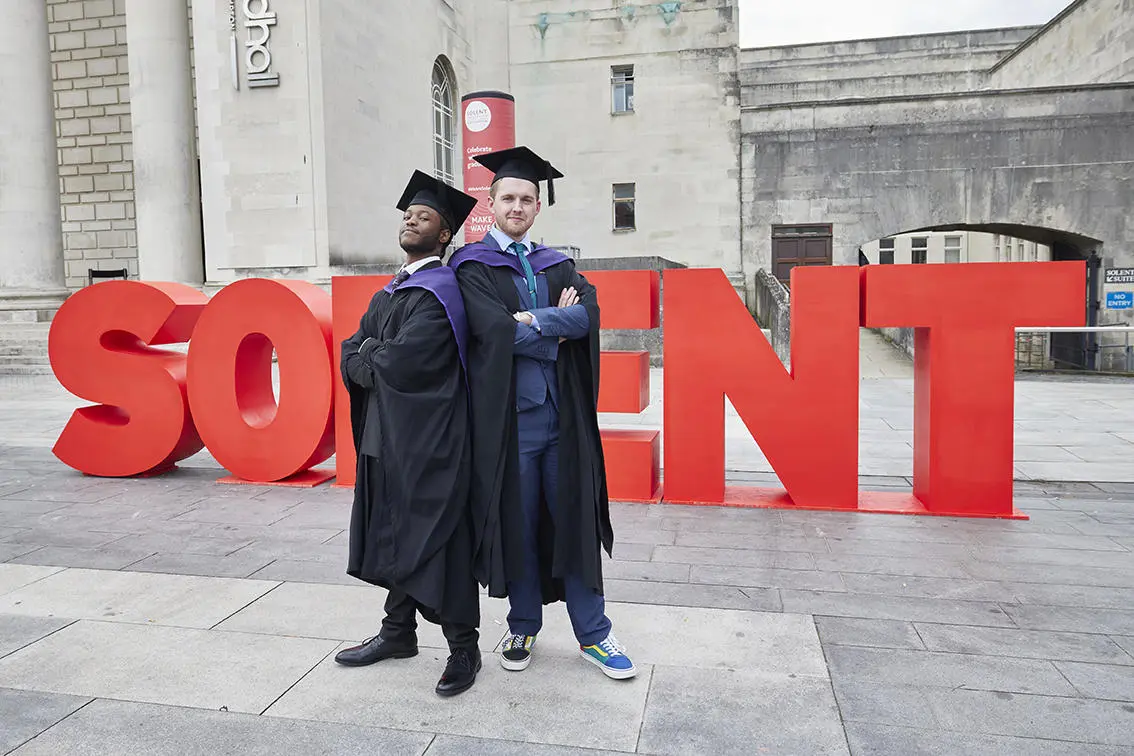 Two students graduating outside a big 'Solent'