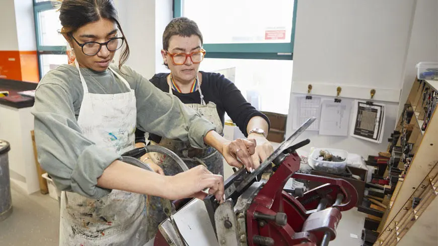 A student with an instructor in the art studios using a print press