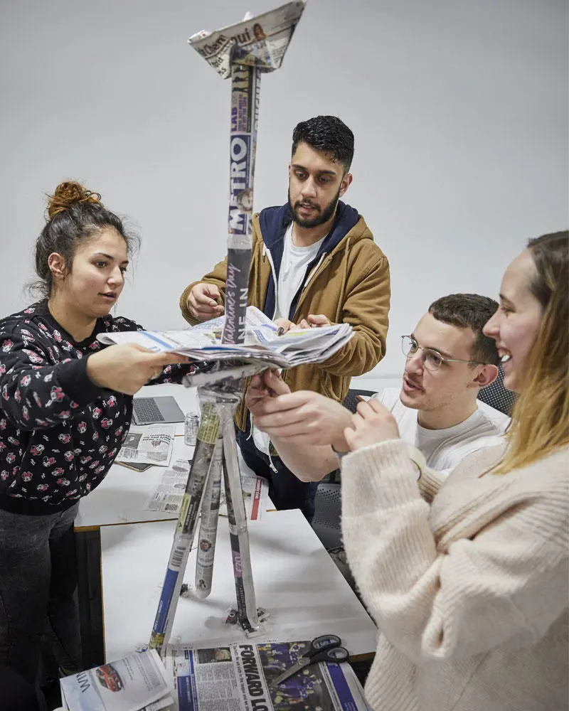 Four students working on a project building a structure out of newspaper