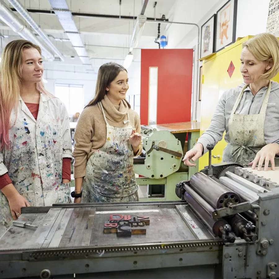 An instructor showing two students how to use a print press