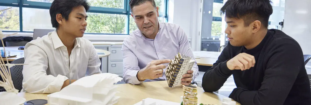 Two architecture students with a course leader looking at 3d models of buildings