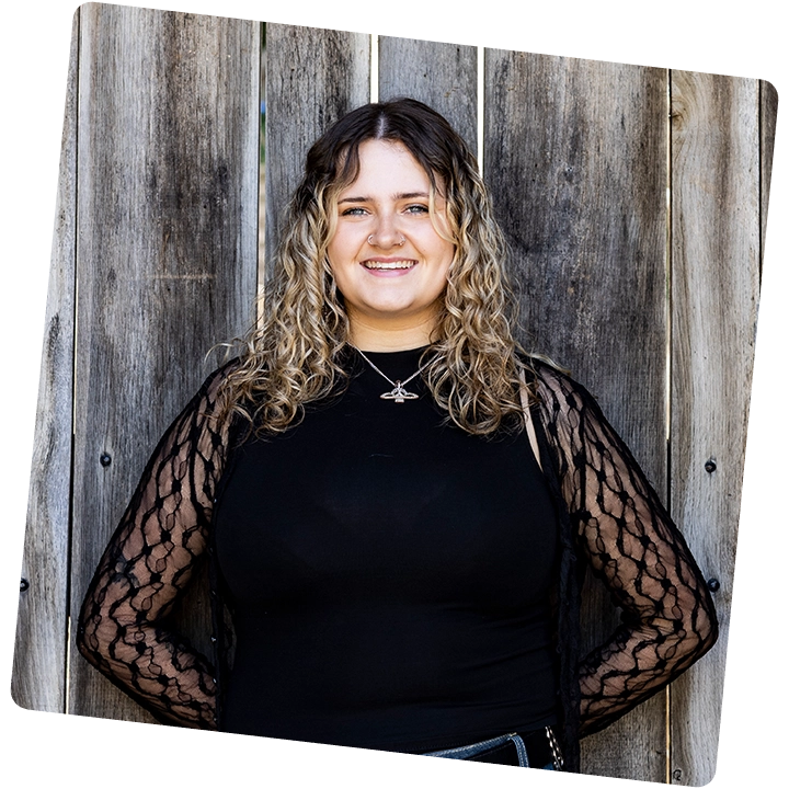 A smiling student stood against a wooden fence