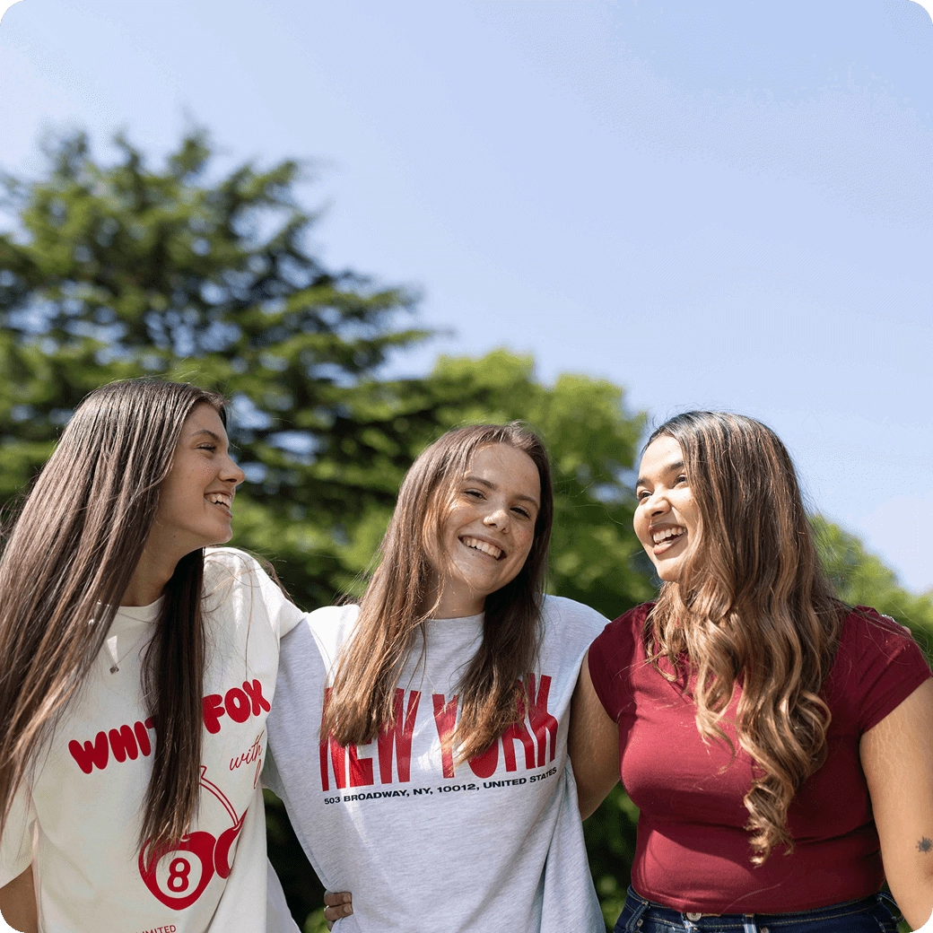 Three female students laughing with each other on a sunny day