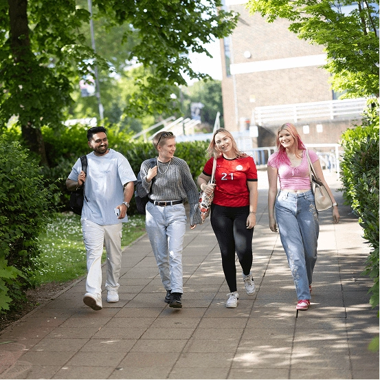 Four smiling students walking through the East Park Terrace campus on a sunny day