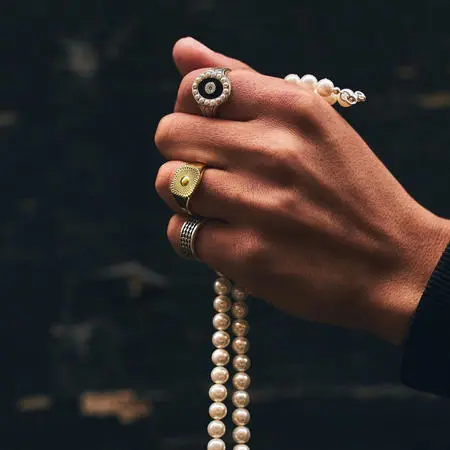 A hand with rings on the fingers holding a string of pearls