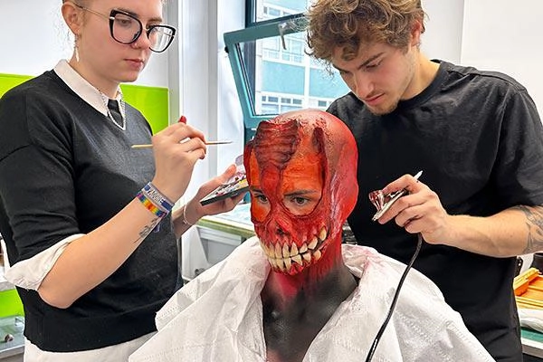Prosthetics students making up a model into a red gory mask