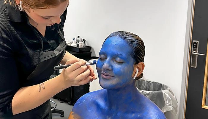 A prosthetics student painting a model's face with blue make up