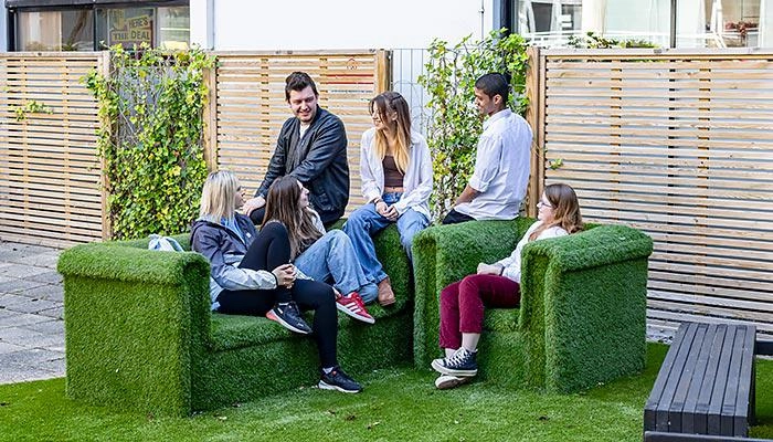 A group of students sitting on outdoor chairs covered in astroturf