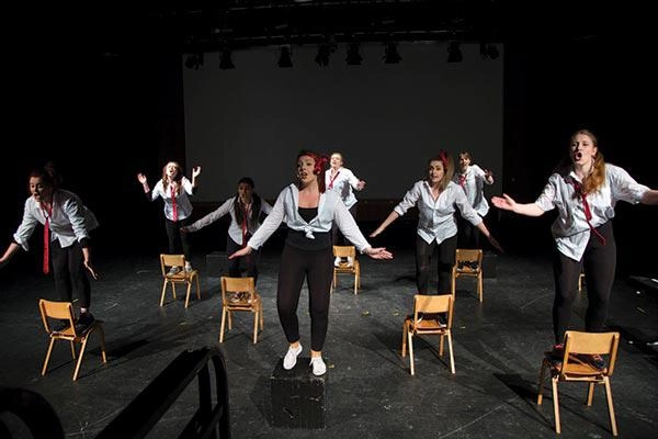 Performing arts students dancing on chairs