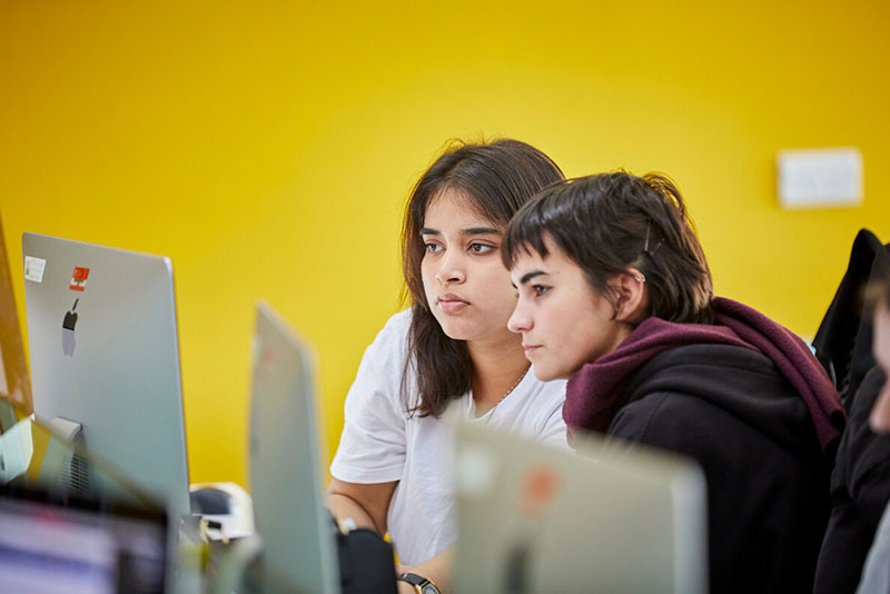 Two creative students looking at a computer monitor