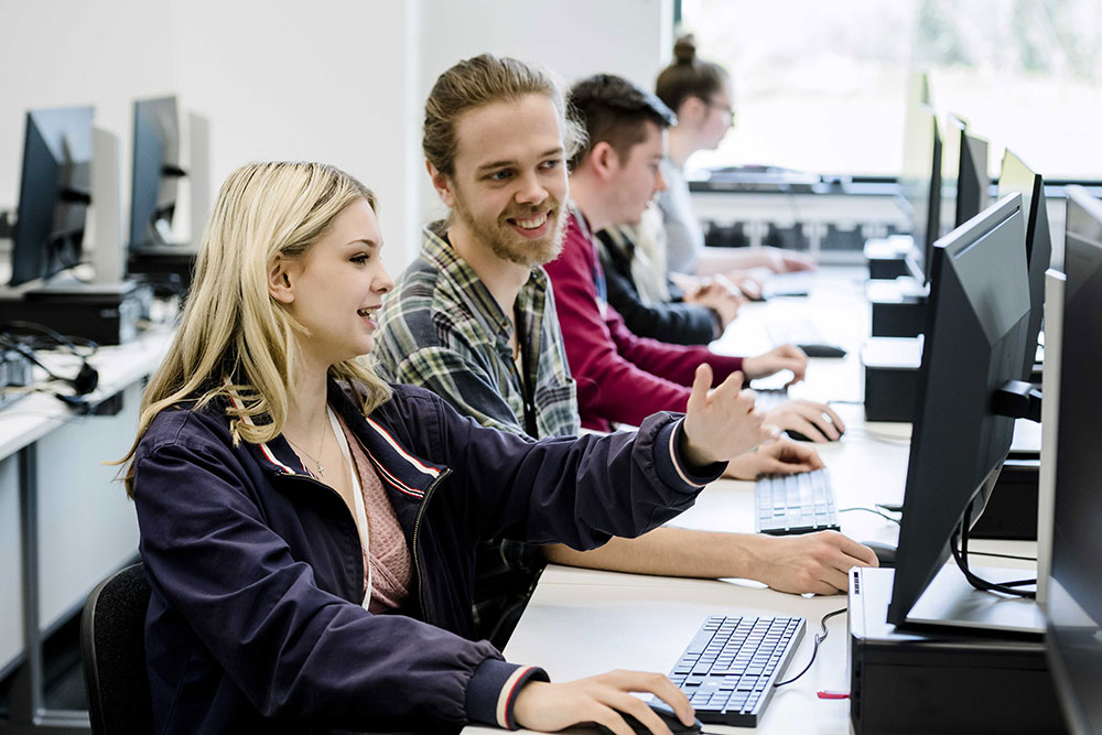 A female student points to a computer monitor while a male student looks on