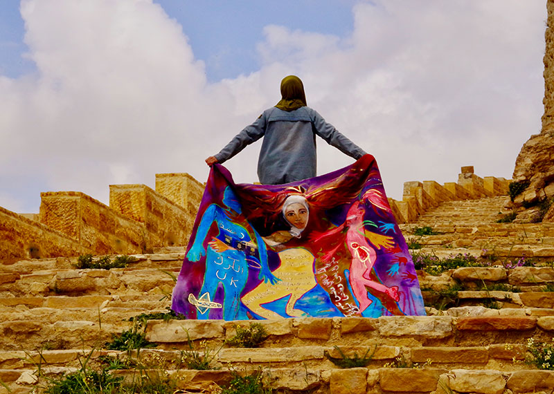 A female refugee holding a piece of artwork on the steps of ancient ruins