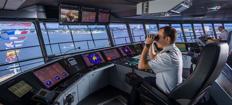 A ship's officer on the bridge of a ship looking through the window with binoculars
