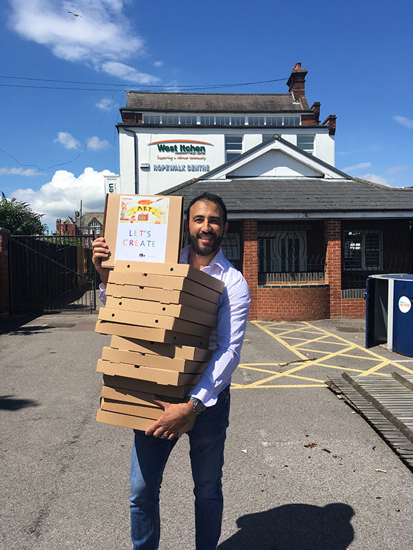 A man holding a stack of art to go pizza boxes