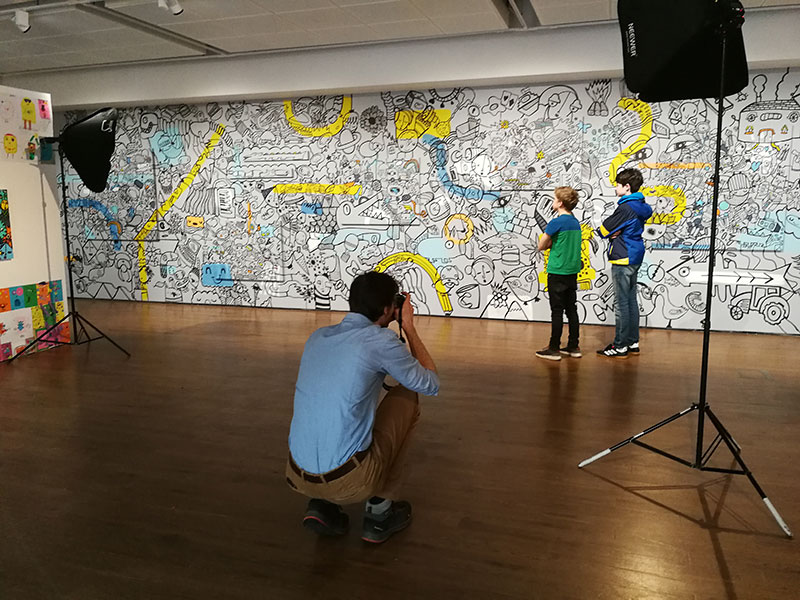 A photographer taking a photo of two children in front of a Kev Munday mural