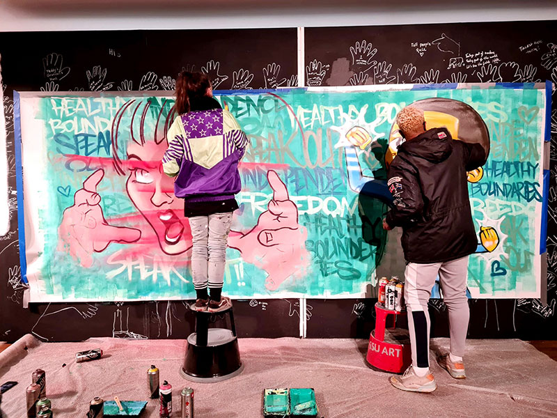 Two people painting a mural on to a wall